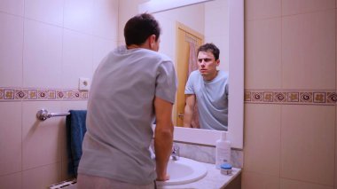 Pazartesi sabahı banyodaki aynada yansımasına bakan bir adam yorgun ve işe gitmek istemiyor.