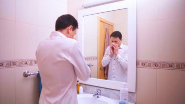 Ofis çalışanı banyo aynasına bakarken burnunu mendille siliyor.