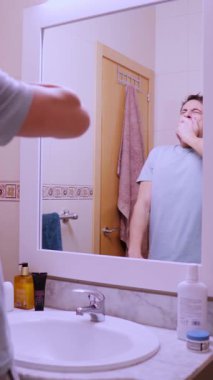 Depresyondaki adam işe gitmek için isteksizce hazırlanıyor, banyo aynasında yansımasıyla yüzleşiyor.