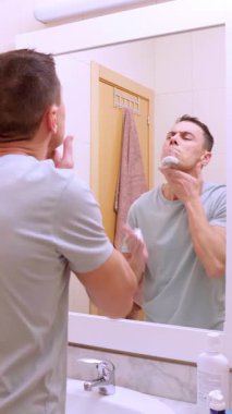 Yüzünde köpük olan bir adam modern bir banyoda tıraş olmaya hazırlanıyor.