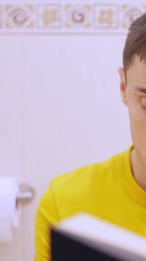 Tuvalette oturup kitap okuyan ve farklı duygular ifade eden bir adam.