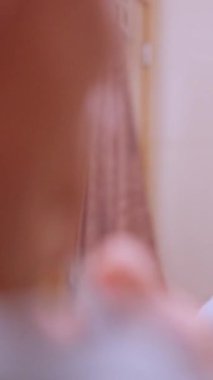 Yetişkin bir adam dişlerini fırçalar ve banyo aynasında kendine bakar.