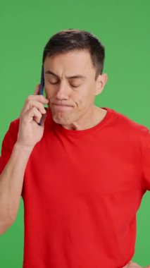 Telefonda çok sinir bozucu ve susmak bilmeyen biriyle konuşan bir adam. Heyecanlanıyor çünkü acelesi var ve telefonu kapatıyor. Orta boy, kırmızı tişört ve yeşil krom anahtar arka plan.