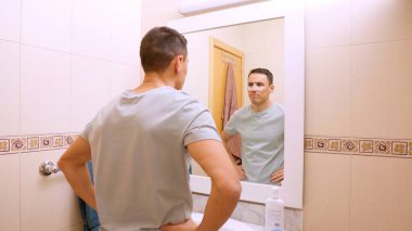 Tenine dikkat eden bir adam banyodaki aynanın önünde siyah halkalar takıyor.