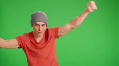 Sarhoş adam bir şişe şarapla mutlu bir şekilde dans ediyor. Orta boy, kırmızı tişört ve yeşil krom anahtar arka plan.