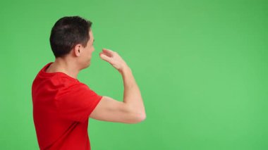 Kırmızı tişörtlü adam krom bir arka planda işaret ediyor, işaret ediyor ve gülümsüyor.