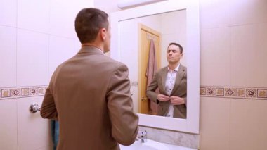 Takım elbisesini ayarlayan ve banyo aynasındaki yansımasına gülümseyen kendine güvenen bir iş adamı.