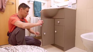 Tesisatçı lavabo sorununu değerlendiriyor ve müşteriyle pahalı tamir çözümlerini tartışıyor.