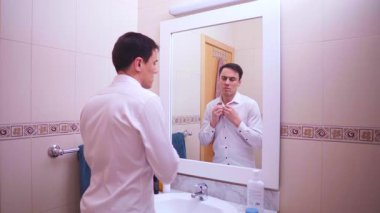 Ofis çalışanı gömleğinin düğmelerini iliklerken depresif bir ifadeyle aynada kendine bakıyor.