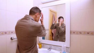 İş adamı aynanın karşısında hazırlanıyor, takım elbisesini ayarlıyor ve parfüm sıkıyor.