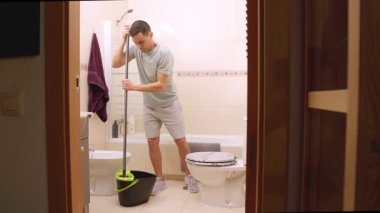 Profesyonel temizlikçi üniformasını giyip banyonun döşemelerini dikkatlice paspaslıyor, temizlik çözeltisini temizlik için kullanıyor ve tuvalet ve küvet civarındaki mikropları temizliyor.