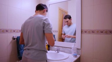 Genç adam banyo aynasının önünde kakao yağıyla dudaklarını nemlendiriyor.