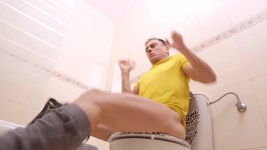 Banyoda tuvalette otururken karın ağrısı çeken bir adam.