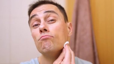 Banyoda yüzünü pamukla temizleyen bir adam.