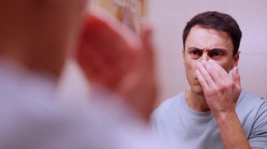 Banyoda aynanın önünde adam yüz kremi sürüyor ve dudaklarına kakao sürüyor.