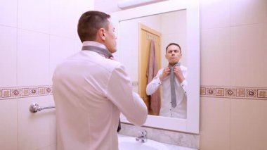 İyimser iş adamı banyodaki aynanın önünde kravatını düzeltiyor.
