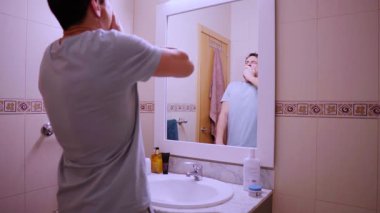 Depresyondaki adam işe gitmek için isteksizce hazırlanıyor, banyo aynasında yansımasıyla yüzleşiyor.