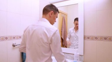 İyimser iş adamı aynada kendine bakıyor, saçını tarıyor ve gülümsüyor.