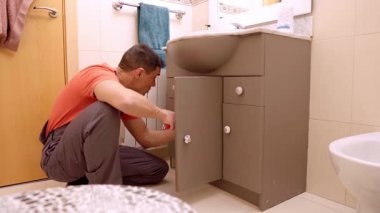 Profesyonel tesisatçı banyo lavabosu dolabını inceliyor ve tamir ediyor.
