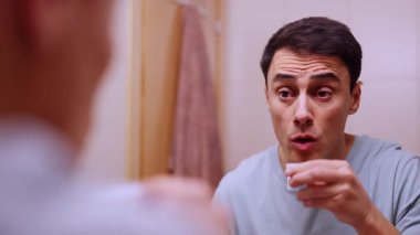 Adam sabah rutini sırasında banyo aynasının önünde gargara yapıyor.