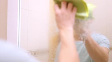 Temizlikçi kirli banyo aynasını sprey ve bezle temizliyor.