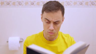 Tuvalette oturup kitap okuyan ve farklı duygular ifade eden bir adam.