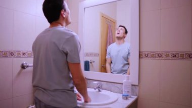 Kendine güveni olmayan bir adam banyodaki aynada saçını tarıyor ve hayal kırıklığına uğramış hissediyor.
