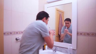 Adam mikrofon olarak diş fırçasını kullanıyor, banyo aynasında enerjik bir şekilde şarkı söylüyor, sabah rutininin tadını çıkarıyor.