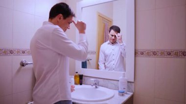 İş adamı endişeyle banyo aynası karşısında konuşma yapıyor ve gerginlik belirtileri gösteriyor.