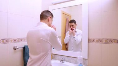 Banyodaki aynada dişlerini temizleyen ve kontrol eden bir iş adamı.