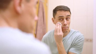 Yakışıklı adam banyoda duştan sonra yüz derisini temizlemek için pamuk pedleri kullanıyor.