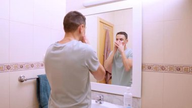 Beyaz adam banyodaki aynanın önünde güzellik tedavisi için göz bandı yapıştırıyor.