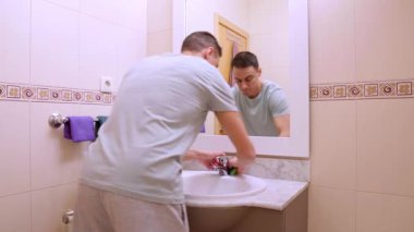 Sıradan kıyafetler giyen bir adam banyoyu ve musluğu dikkatlice temizliyor.