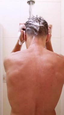 Adam sırtüstü yatmış, duş alırken saçlarını şampuanla ovalıyor.