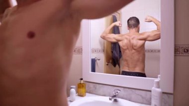 Gömleksiz bir adam banyo aynasında sırt kaslarına hayran.