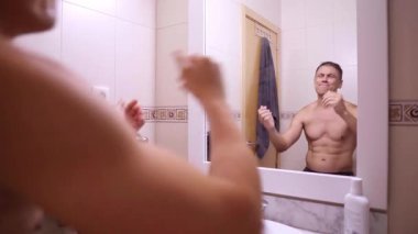 Üstsüz adam kendini kontrol ediyor, banyo aynasının önünde dans ediyor ve esniyor.