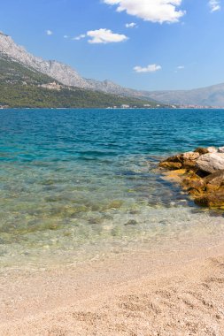 Korcula Island coastline featuring clear sea water merging with a sandy shore and distant mountains
