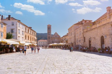 Güneşli bir günde Hırvatistan 'ın Hvar kentindeki St. Stephens Meydanı' nda yürüyen ve dinlenen insanlar