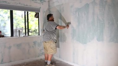 İşçi süreç macunu alçıpan üzerine serpiştirir macunu elle bitirir bir spatula.