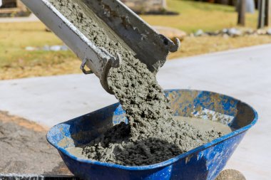 Beton karıştırıcı kamyon inşaat alanında mavi el arabasına ıslak çimento döküyor.