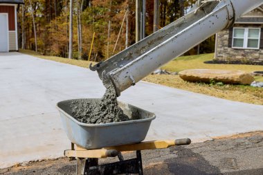 Concrete mixer truck pours wet cement into wheelbarrow during construction on construction site clipart