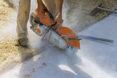 İnşaat işçisi beton kaldırımı kesmek için elmas testeresi kullanıyor.