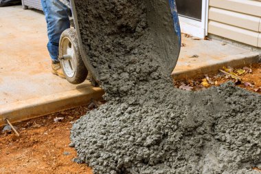 İnşaat işçisi, el arabasından çimento kullanarak evin yan tarafına beton kaldırım döker.