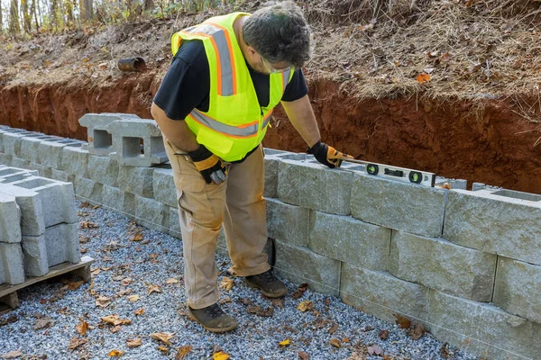 stock image Man leveling tool building retaining concrete block wall with being built on new property