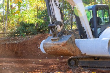 Yerdeki beton kanalizasyon borularını kaldırmak için traktör kullanan işçiler yeraltı tesisi için hazırlanıyorlar.