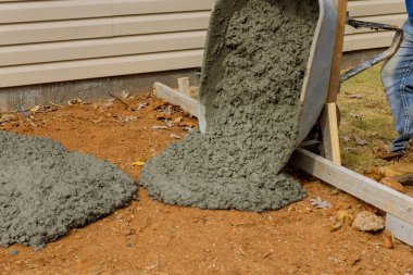 İnşaat işçisi, gelecekte kullanılacak beton kaldırımlar için el arabasından çimento döküyor.