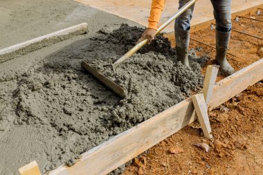 İşçiler inşaat ekibi tarafından evin yan tarafına inşa edilecek ek bir kaldırım yaratmak için çimento döküyorlar.