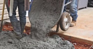 İnşaat işçisi yan evde beton kaldırım yaratmak için el arabasından çimento döküyor.