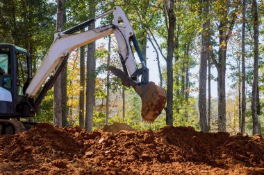 İnşaat alanında, orman kovasının yanında bir kazıcı toprak kazıyor.