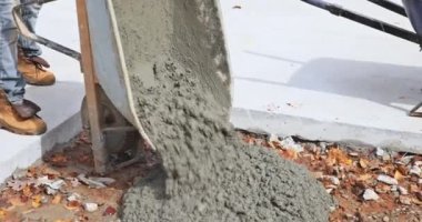 İnşaat işçisi el arabasından eve yeni kaldırımlar yapmak için çimento döküyor.